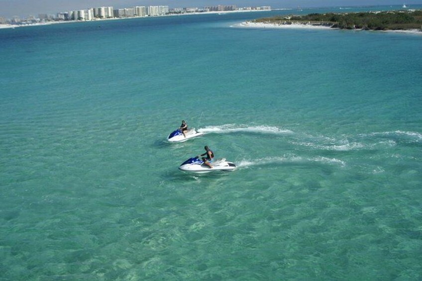 Two jet skis on a clear turquoise sea with a distant shoreline and buildings. 3