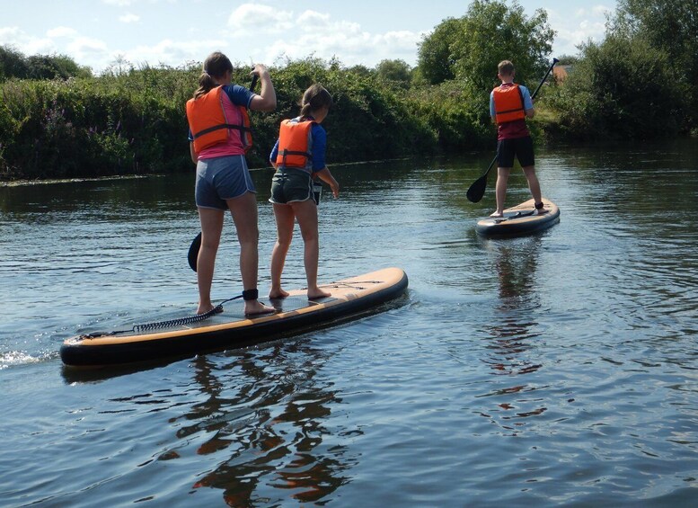 Three people on paddleboards in a calm river surrounded by greenery. 5