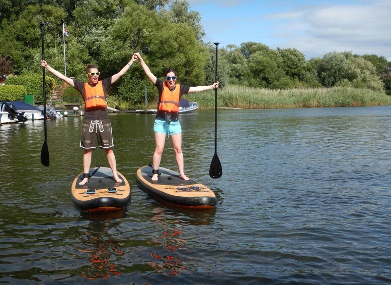 Two people stand-up paddleboarding on a calm lake with trees in the background. 3