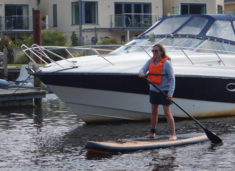 A person paddleboarding on a calm body of water with a boat docked nearby. 4