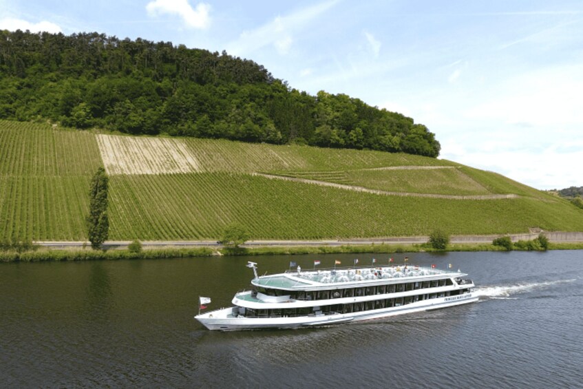 A river cruise boat on a river with a forested hillside in the background. 1