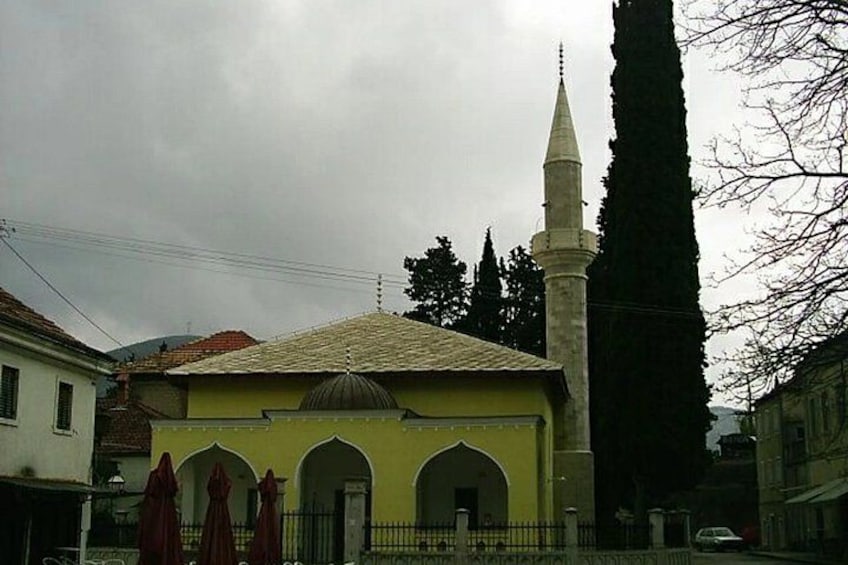 A mosque with a minaret, a yellow facade, and arched doorways. 5