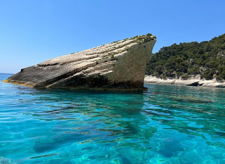 A large rock formation in clear turquoise waters with a sandy beach and dense greenery in the background. 5
