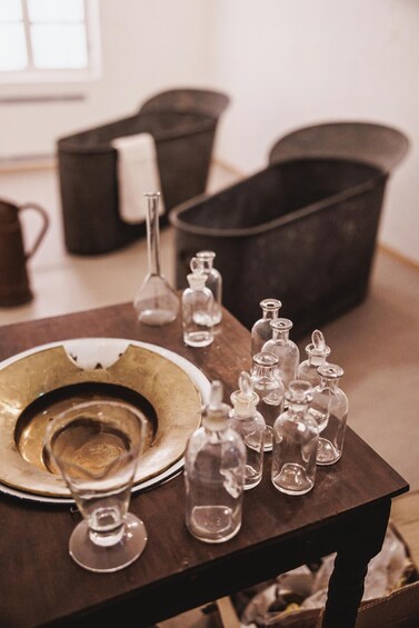 A table with a brass plate, a wine glass, and several glass bottles. 3