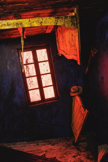 A rustic room with a window, wooden walls, and a hat hanging on the wall. 5