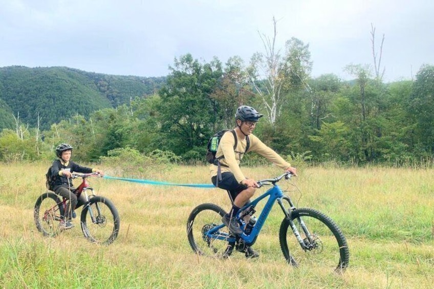 Two cyclists on a trail with a forested hill in the background. 4