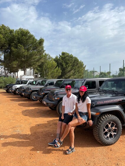 Two people sitting on a Rubicon SUV in a parking lot with multiple Rubicon SUVs lined up. 3