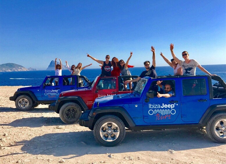 Three blue off-road vehicles with 'Ibiza Jeep' branding parked on a sandy beach with the ocean and a clear sky in the background. 1