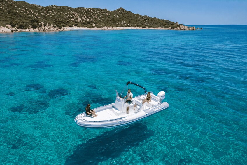 A boat on clear turquoise water with a rocky coastline in the background. 1