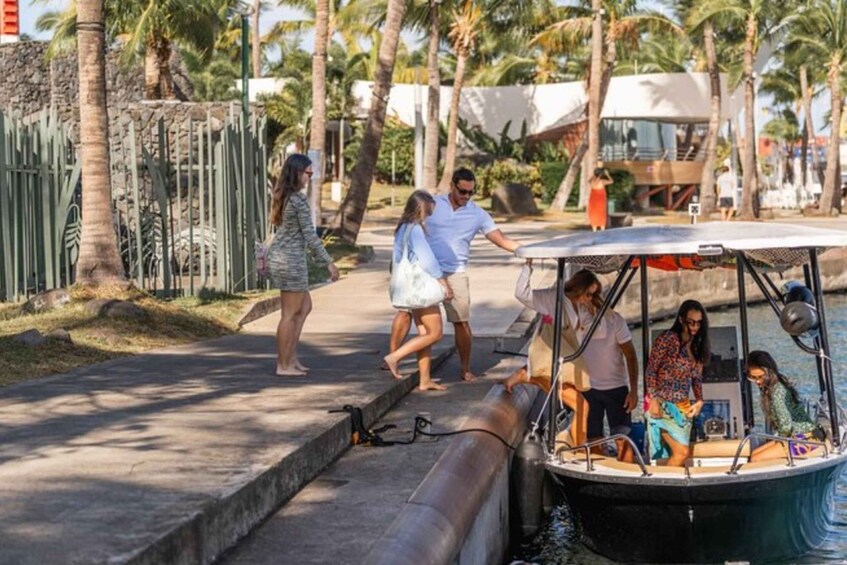 A group of people on a boat docked at a marina with palm trees and a stone wall in the background. 3