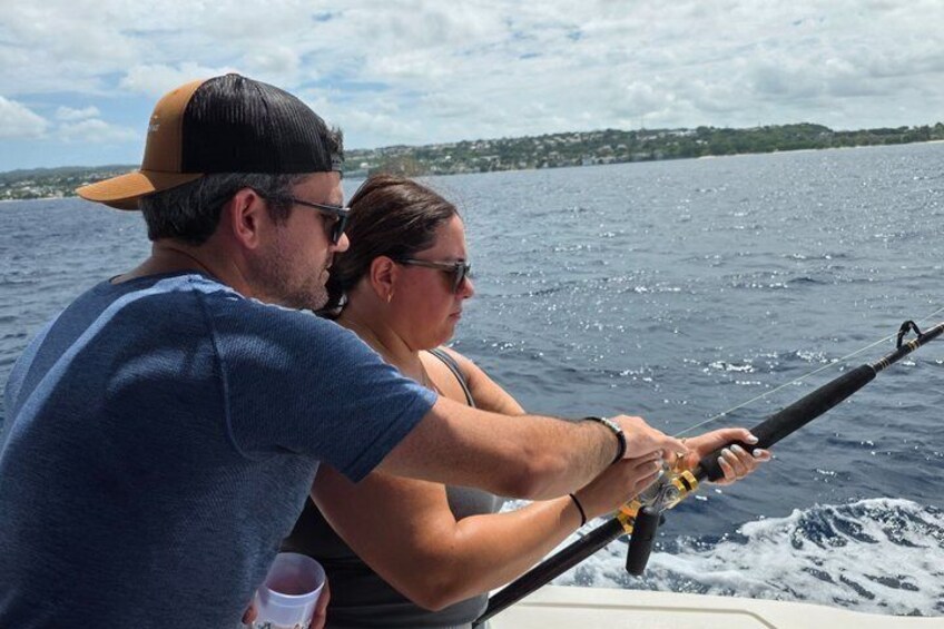 Two people fishing on a boat with a calm sea and a distant shoreline. 5
