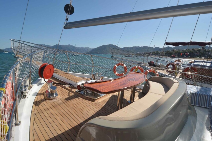 A yacht deck with lifebuoys, a steering wheel, and a view of the sea and mountains. 2