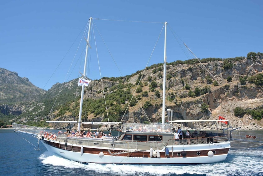 A boat with passengers on a clear day, sailing near rocky cliffs. 1