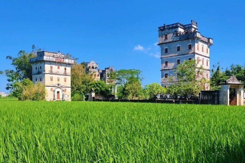 A historical building complex with a tower, surrounded by a lush green field. 1