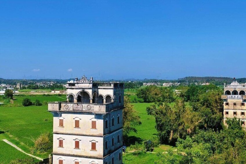 A multi-tiered tower with arched windows and a dome, surrounded by lush greenery and fields. 2
