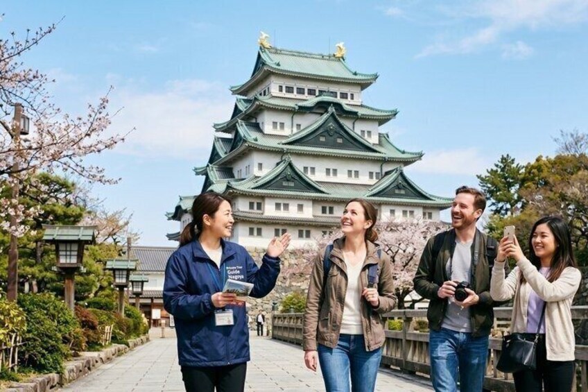 A group of people standing in front of a traditional Japanese castle with cherry blossoms. 1