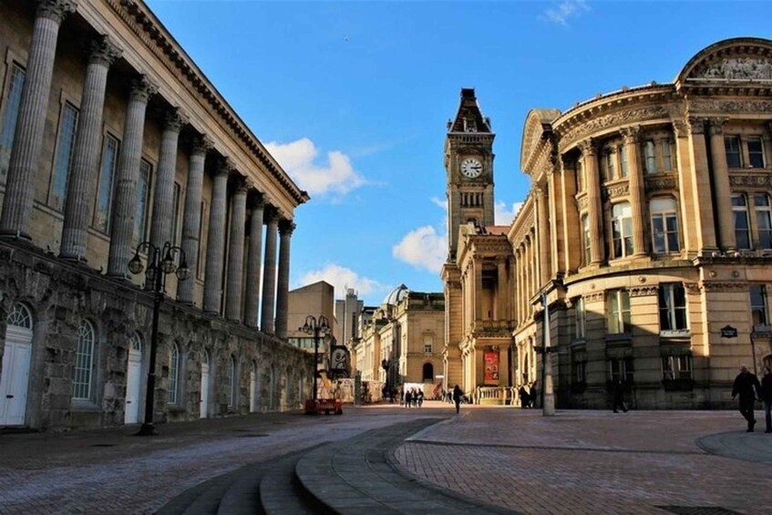 A historic square with classical architecture, a prominent clock tower, and a cobblestone street. 1