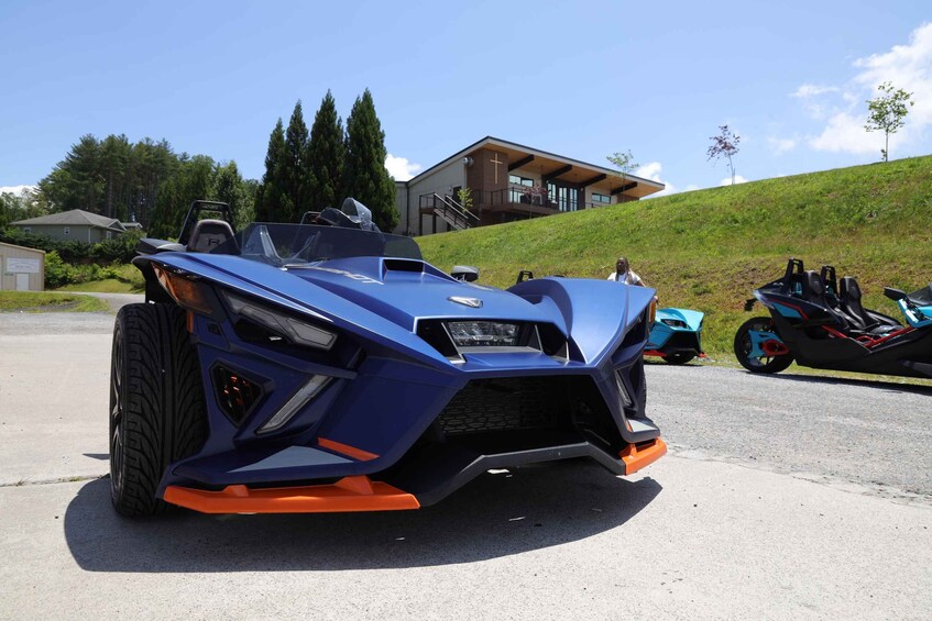 A blue sports car parked on a street with a house and trees in the background. 2