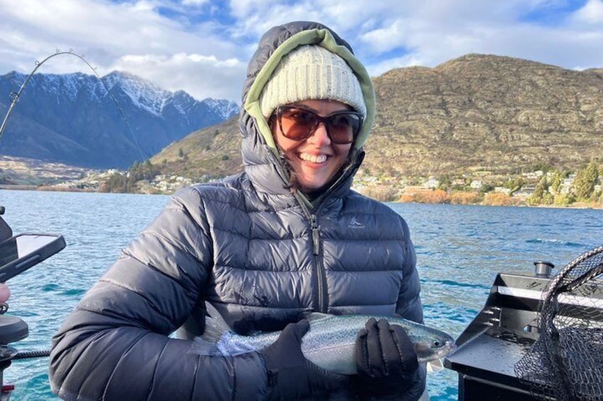 A person holding a fish on a boat with mountains in the background. 3