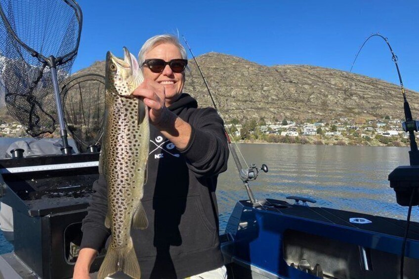 A person holding a fish on a boat with a net and fishing rod in the background. 1