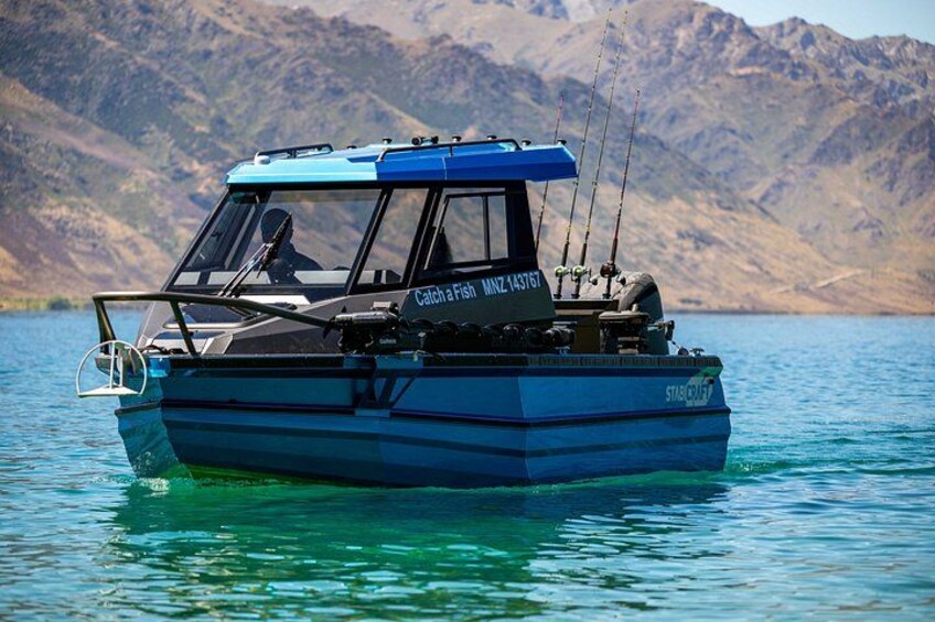 A blue fishing boat named 'Catch a Fish' on calm water with mountains in the background. 2