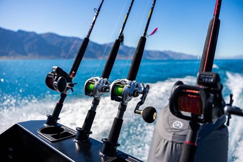 Fishing rods, a fishing reel, and a digital device on a boat with a mountainous landscape in the background. 5