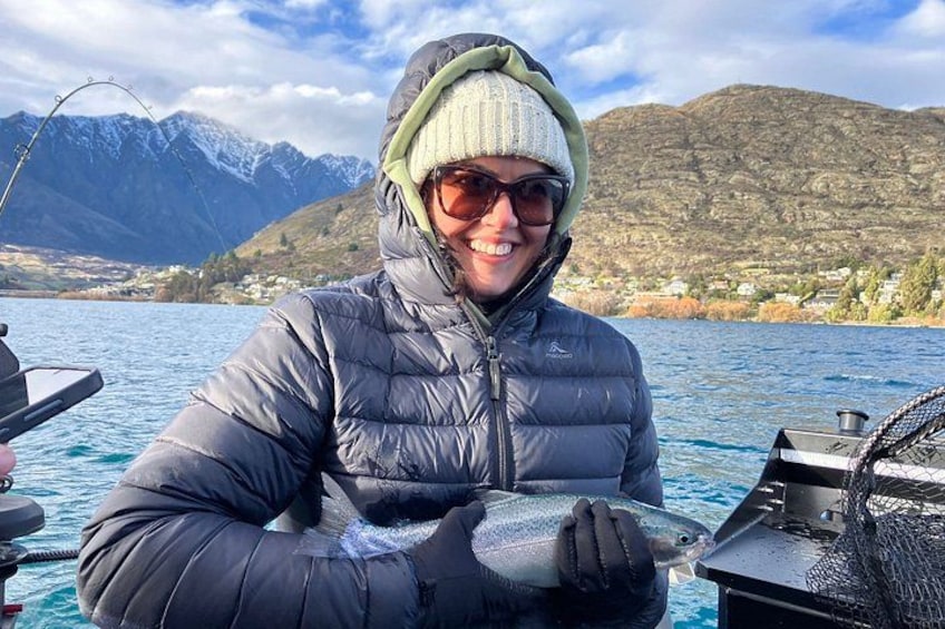 A person holding a fish on a boat with mountains in the background. 3