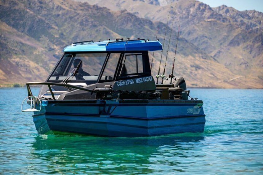 A blue fishing boat named 'Catch a Fish' on calm water with mountains in the background. 2