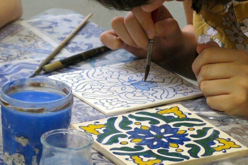 A person painting a tile with a blue and yellow floral design. 1