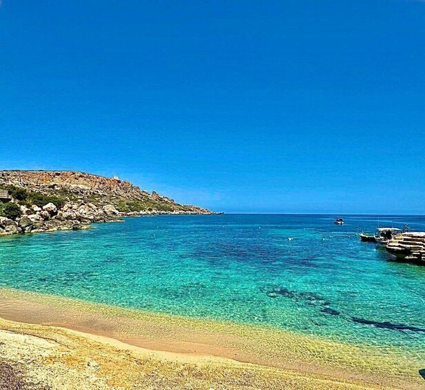 A clear blue sea, rocky coastline, and a pier with boats. 5