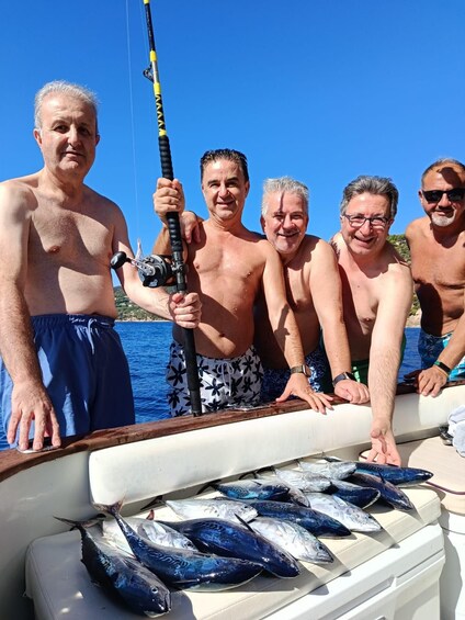 A group of people on a boat with fishing rods, holding a large fish. 4