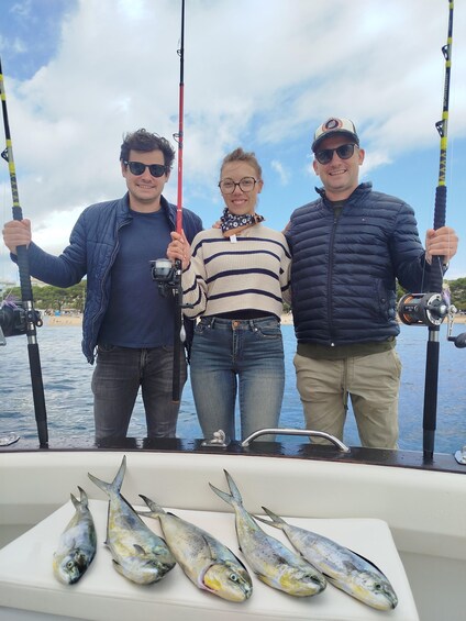 Three people on a boat holding fishing rods, with several fish on the boat's deck. 4