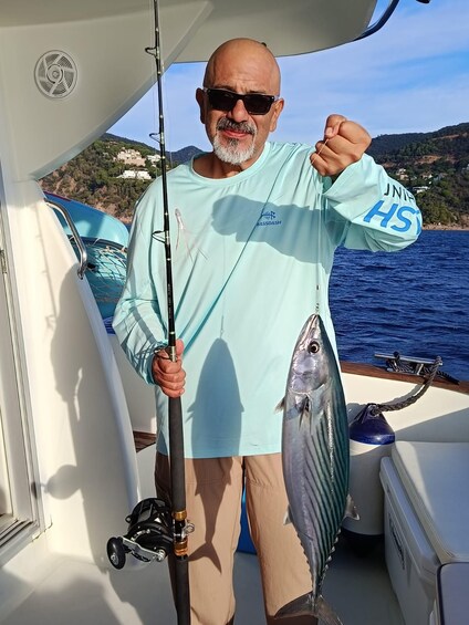 A person on a boat holding a fish, with a fishing rod and a cooler visible. 2