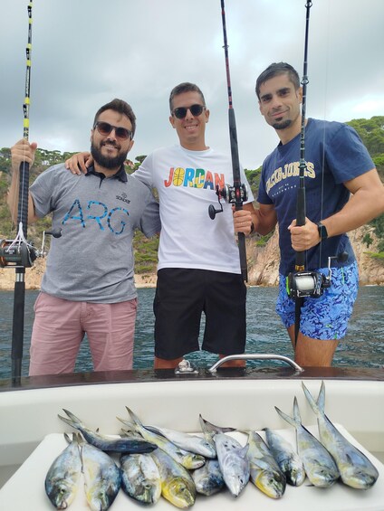 Three people fishing on a boat with several fish on the deck. 1