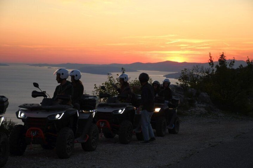 A group of people on ATVs at sunset with a view of the water and mountains. 3