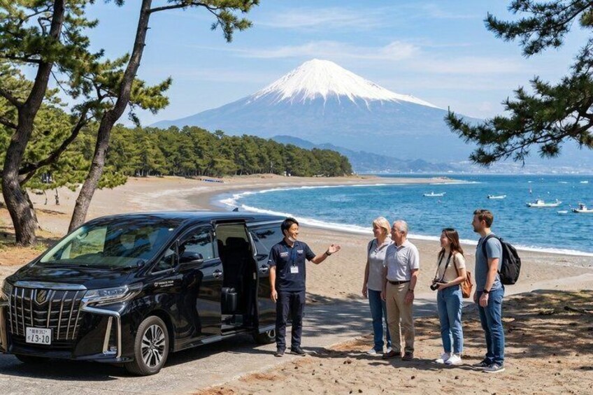 A black van parked on a beach with a group of people standing beside it, a mountain in the background, and the ocean with boats. 1