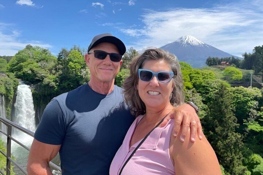 A couple standing by a waterfall with a mountain in the background. 2