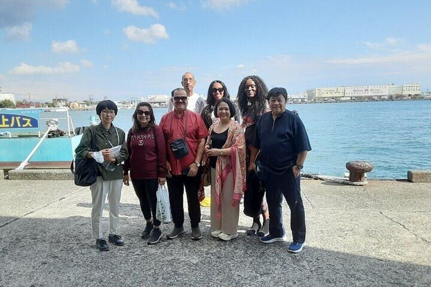 A group of people standing on a waterfront promenade with a boat docked in the background. 4