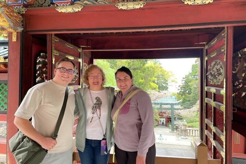 Three people standing in a traditional wooden structure with ornate carvings. 3