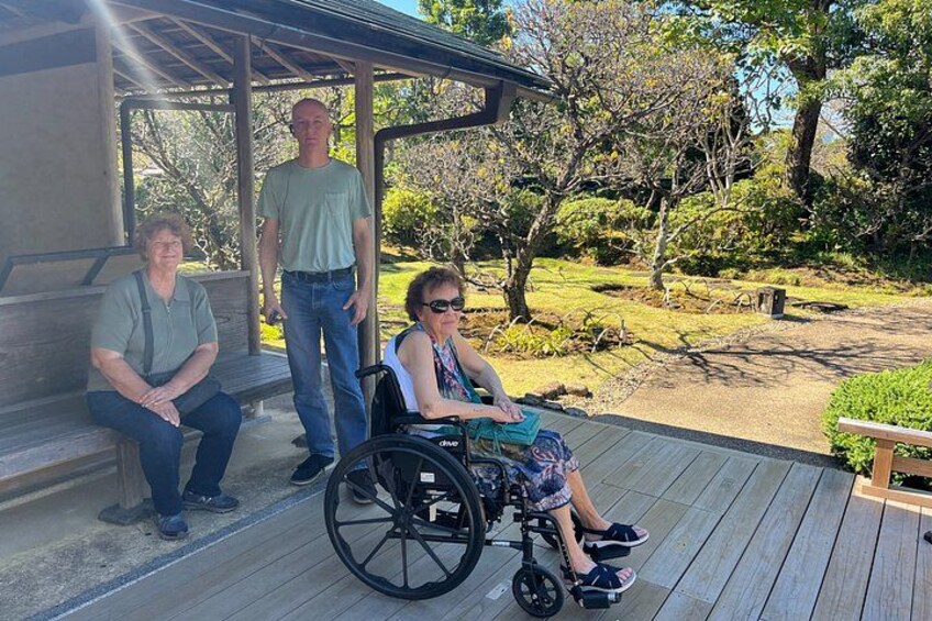 A person in a wheelchair on a wooden deck, another person standing, and a third person sitting. 2