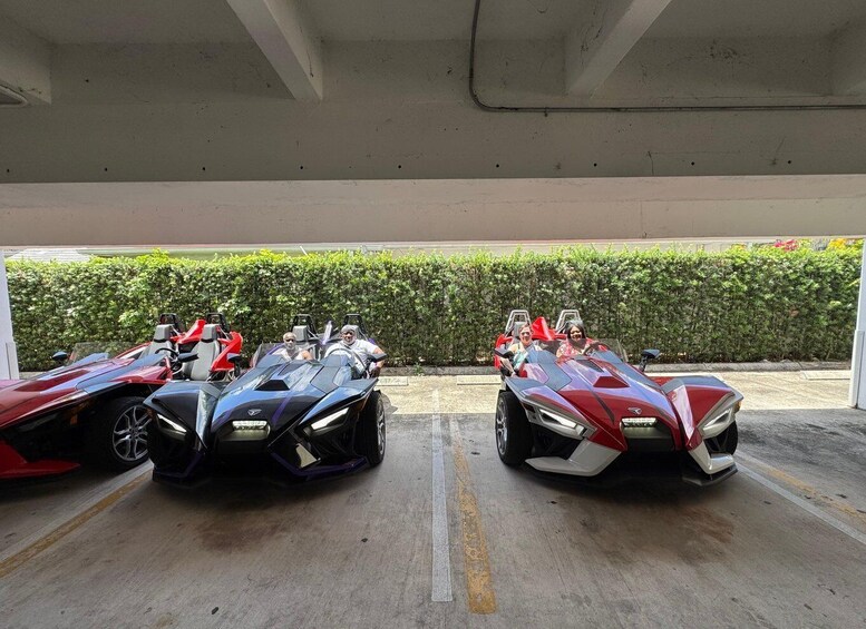 Three futuristic race cars parked in a covered area with a hedge in the background. 4