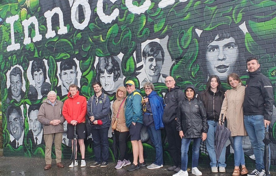 A group of people standing in front of a mural with the word 'Innocent' and faces of various individuals. 5