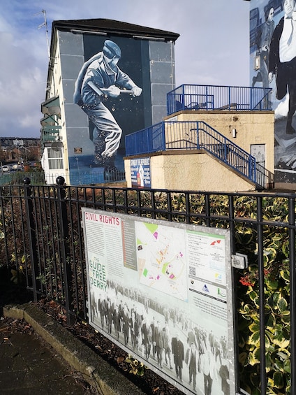 A mural of a man in a suit, a staircase, and a signboard with historical information. 4