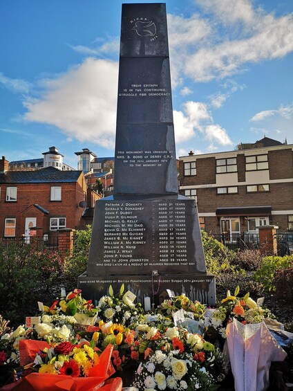 A memorial monument with a list of names and ages, surrounded by flowers. 2