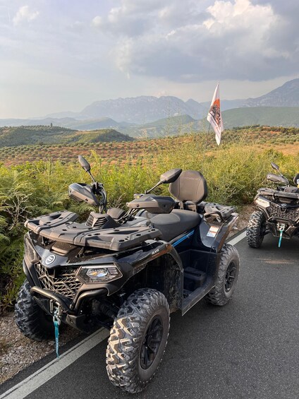 Two ATVs parked on a road with a mountainous landscape in the background. 2