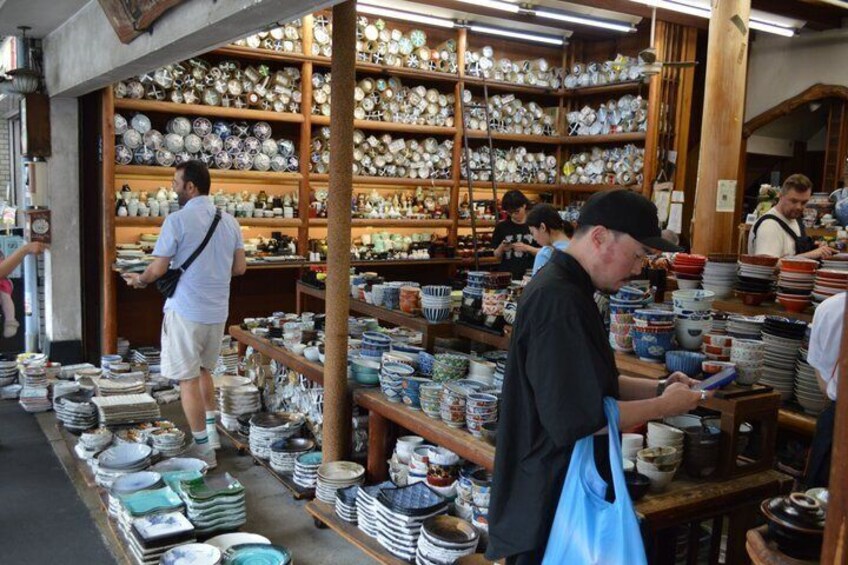 A pottery shop with shelves of ceramic dishes and a man examining items. 4