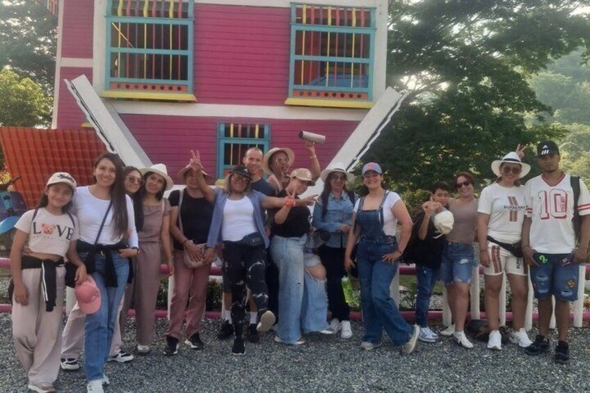A group of people posing in front of a colorful house with a red and pink facade and blue trim. 1