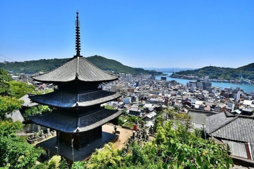 A traditional Japanese pagoda with multiple tiers, surrounded by lush greenery and overlooking a coastal cityscape. 2