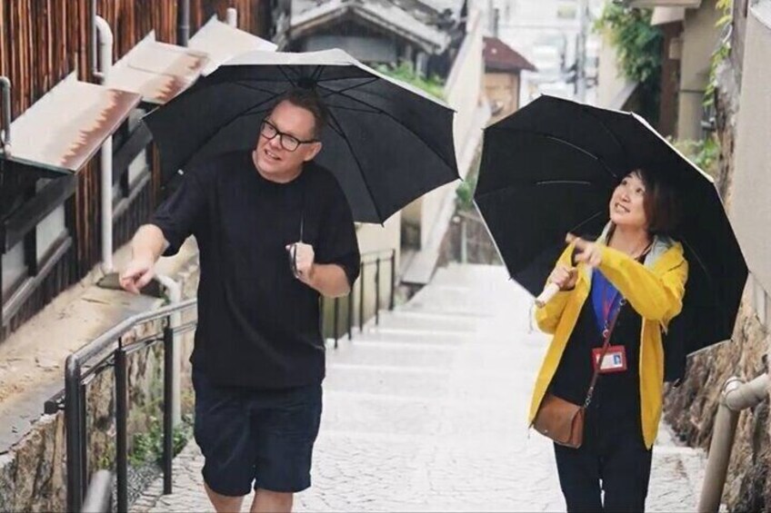 Two people walking down a cobblestone street, one holding a black umbrella and the other a yellow umbrella. 1