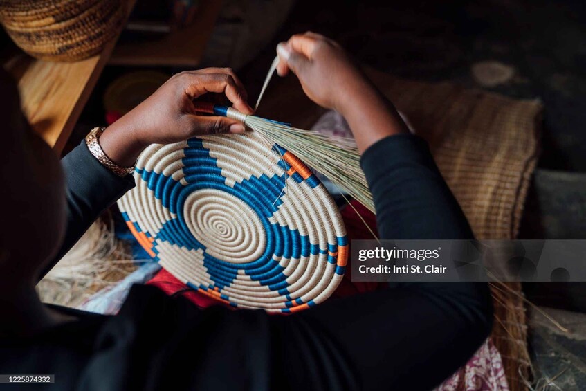 A person weaving a circular basket with blue and beige strips. 2